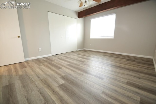 unfurnished bedroom featuring beam ceiling, a closet, light hardwood / wood-style floors, and ceiling fan