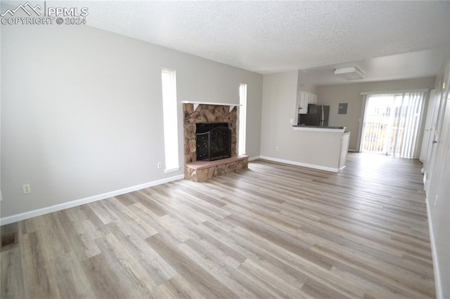 unfurnished living room with a stone fireplace, a textured ceiling, and light hardwood / wood-style flooring