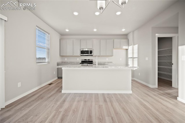 kitchen with light stone counters, a center island with sink, stainless steel appliances, and light hardwood / wood-style floors