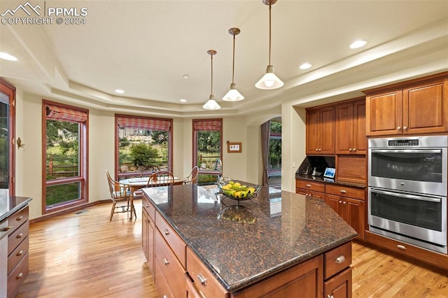 kitchen featuring light hardwood / wood-style floors, a tray ceiling, stainless steel double oven, and a kitchen island