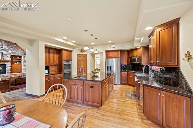 kitchen featuring light wood-type flooring, backsplash, a kitchen island with sink, appliances with stainless steel finishes, and sink