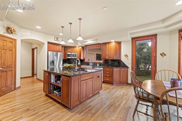 kitchen featuring stainless steel appliances, a center island with sink, sink, decorative backsplash, and light wood-type flooring