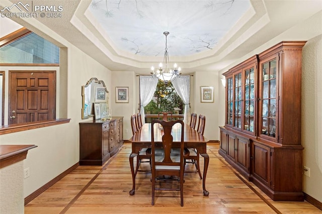 dining area featuring light hardwood / wood-style floors, a raised ceiling, and a notable chandelier