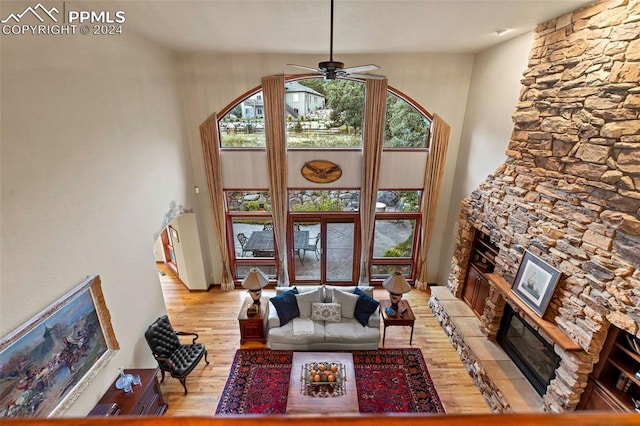 living room featuring light hardwood / wood-style floors, a healthy amount of sunlight, a stone fireplace, and ceiling fan