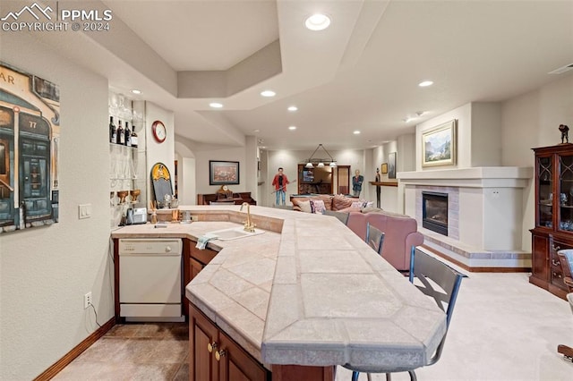 kitchen featuring a fireplace, sink, white dishwasher, a breakfast bar area, and light tile patterned floors