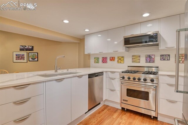 kitchen with appliances with stainless steel finishes, light wood-type flooring, sink, white cabinetry, and light stone counters