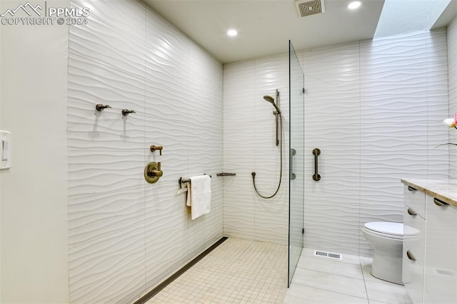 bathroom with tile walls, toilet, vanity, tile patterned flooring, and a shower with shower door