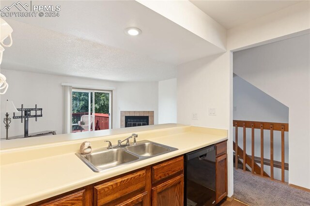 kitchen featuring light carpet, sink, a fireplace, and black dishwasher