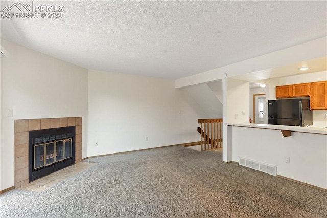 unfurnished living room featuring light colored carpet, a tile fireplace, and a textured ceiling