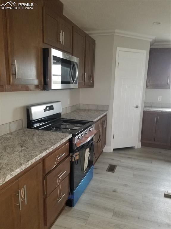 kitchen featuring black range with gas stovetop, light hardwood / wood-style floors, light stone counters, and ornamental molding