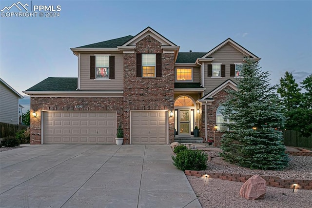 traditional-style house with an attached garage, a shingled roof, concrete driveway, and brick siding