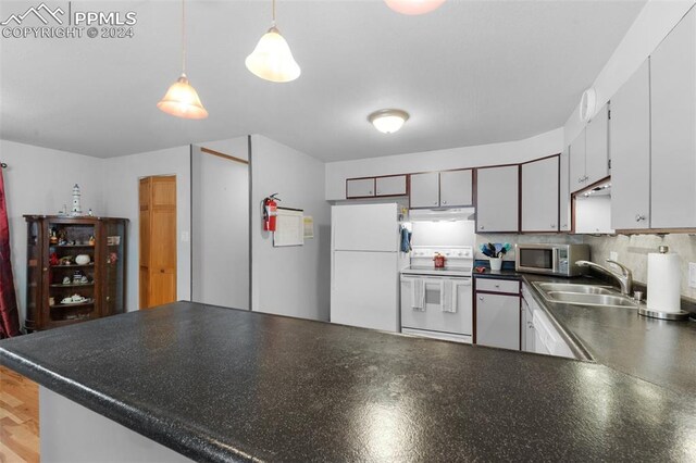 kitchen with decorative light fixtures, white appliances, sink, tasteful backsplash, and kitchen peninsula