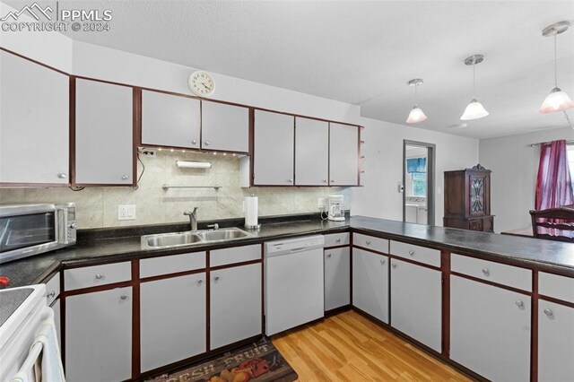 kitchen featuring light wood-type flooring, backsplash, white dishwasher, sink, and decorative light fixtures