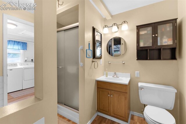 bathroom with toilet, hardwood / wood-style floors, a shower with shower door, washing machine and clothes dryer, and vanity