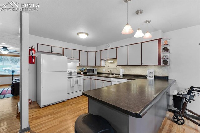 kitchen with decorative backsplash, kitchen peninsula, pendant lighting, light wood-type flooring, and white appliances