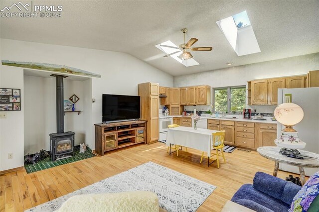 kitchen featuring ceiling fan, light brown cabinets, vaulted ceiling with skylight, a wood stove, and light hardwood / wood-style flooring