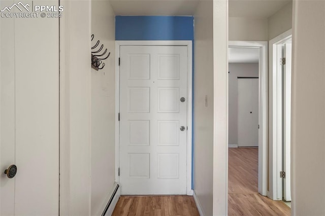 hallway featuring a baseboard heating unit, light wood finished floors, and baseboards