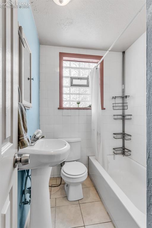 bathroom featuring tile walls, tile patterned flooring, toilet, a textured ceiling, and shower / bath combo with shower curtain