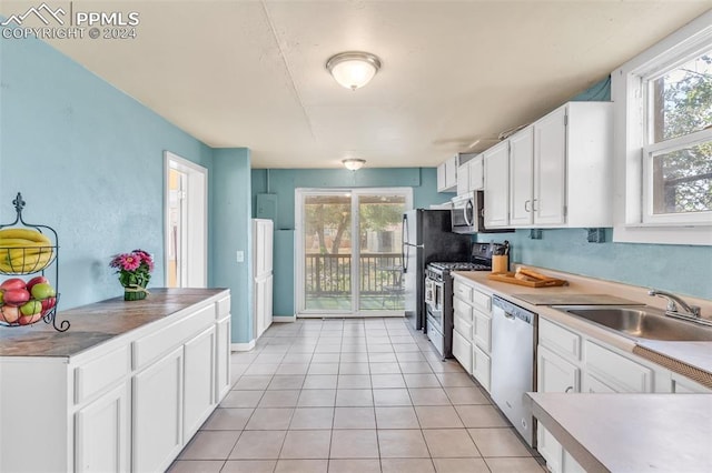 kitchen featuring light tile patterned flooring, white cabinetry, sink, stainless steel appliances, and a healthy amount of sunlight