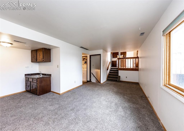 unfurnished living room featuring a wealth of natural light, sink, and carpet floors