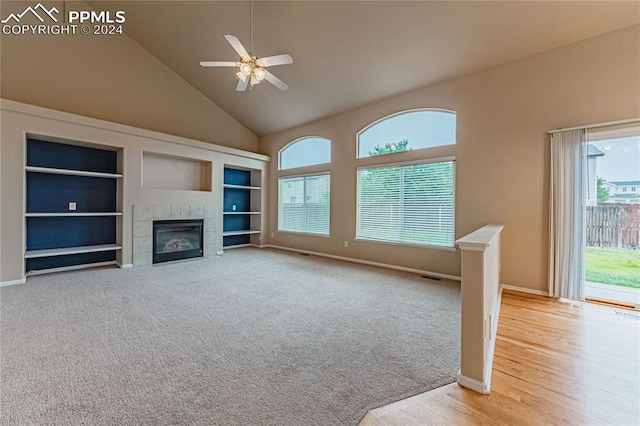 unfurnished living room with a wealth of natural light, ceiling fan, a tiled fireplace, and high vaulted ceiling