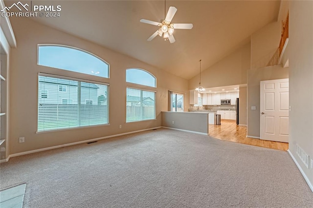 unfurnished living room featuring ceiling fan with notable chandelier, light carpet, and high vaulted ceiling