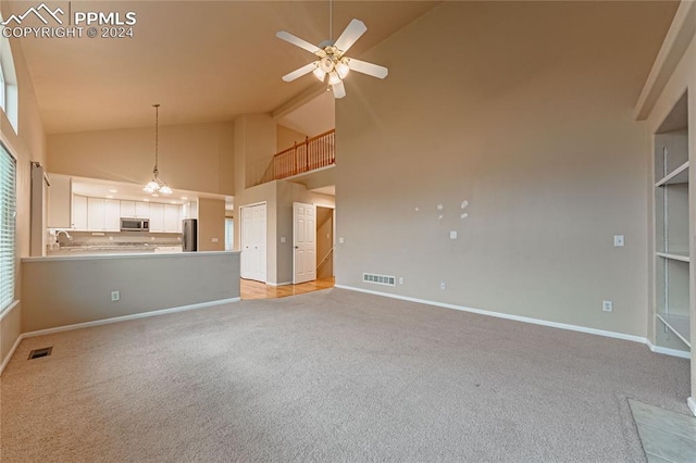 unfurnished living room featuring light colored carpet, sink, ceiling fan with notable chandelier, and high vaulted ceiling