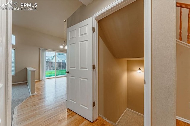 corridor with vaulted ceiling, a notable chandelier, and light hardwood / wood-style floors