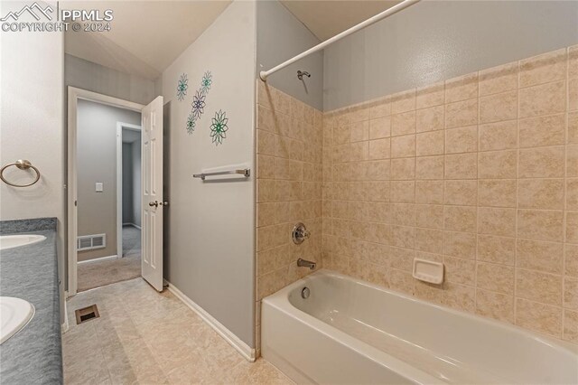 bathroom featuring tile patterned flooring, tiled shower / bath combo, vaulted ceiling, and vanity