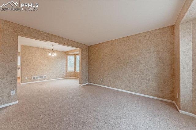 carpeted empty room with an inviting chandelier