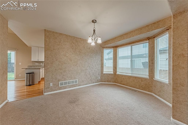 carpeted spare room featuring lofted ceiling and an inviting chandelier