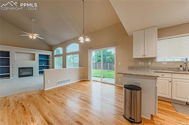 kitchen featuring white cabinets, a tiled fireplace, light hardwood / wood-style flooring, ceiling fan with notable chandelier, and light stone countertops