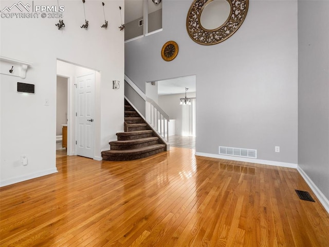 unfurnished living room featuring an inviting chandelier, wood-type flooring, and a high ceiling