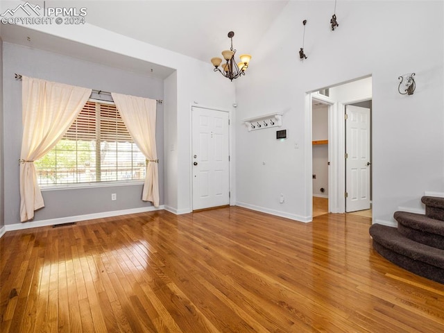 unfurnished living room with high vaulted ceiling, wood-type flooring, and an inviting chandelier