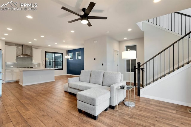 living room featuring light hardwood / wood-style floors, ceiling fan with notable chandelier, and sink