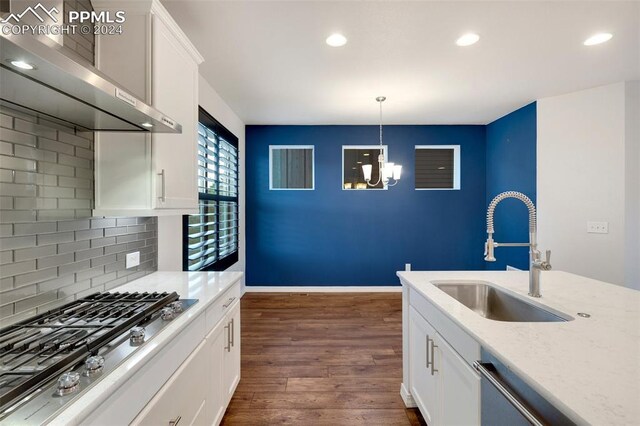 kitchen with wall chimney range hood, backsplash, dark hardwood / wood-style flooring, white cabinets, and sink