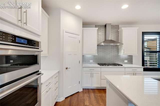 kitchen with backsplash, stainless steel appliances, wall chimney range hood, white cabinets, and wood-type flooring