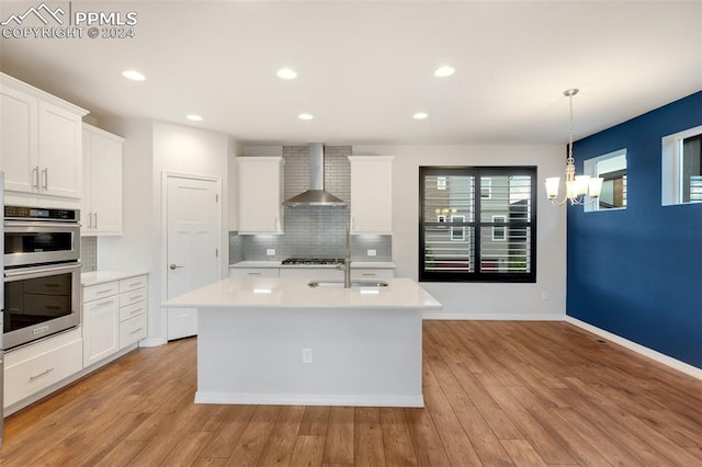 kitchen with stainless steel appliances, decorative backsplash, white cabinetry, wall chimney exhaust hood, and light wood-type flooring