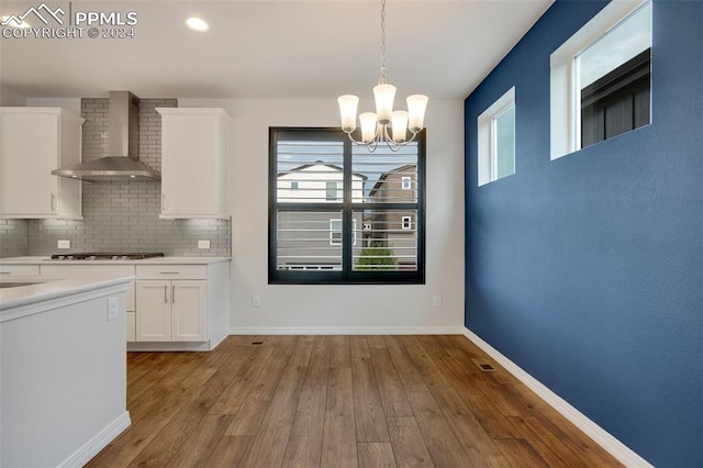 kitchen with backsplash, light hardwood / wood-style floors, white cabinetry, a chandelier, and wall chimney exhaust hood