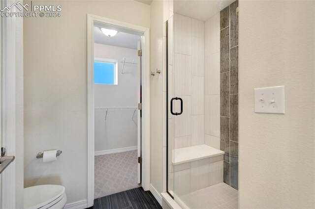 bathroom with a shower with door, toilet, and tile patterned floors