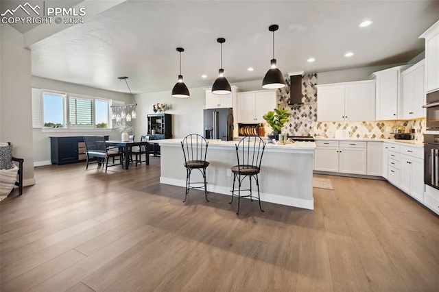 kitchen with hanging light fixtures, white cabinetry, high quality fridge, and a center island with sink