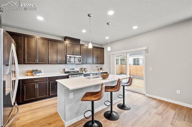 kitchen with a kitchen island with sink, hanging light fixtures, sink, tasteful backsplash, and appliances with stainless steel finishes