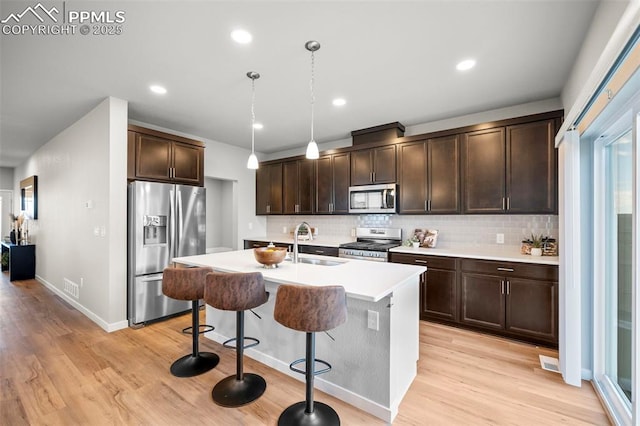 kitchen featuring appliances with stainless steel finishes, sink, hanging light fixtures, dark brown cabinetry, and a kitchen island with sink