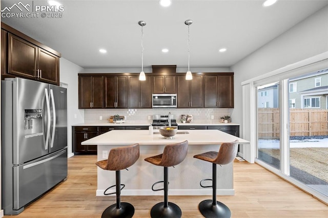 kitchen featuring appliances with stainless steel finishes, hanging light fixtures, dark brown cabinetry, and a breakfast bar area