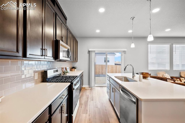 kitchen with hanging light fixtures, stainless steel appliances, sink, backsplash, and dark brown cabinets