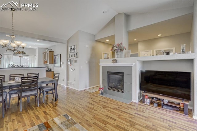 living room with high vaulted ceiling, an inviting chandelier, light hardwood / wood-style flooring, and a tiled fireplace