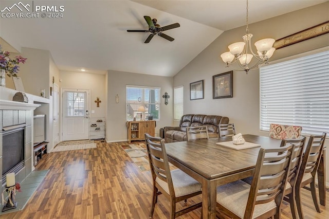 dining space featuring ceiling fan with notable chandelier, wood-type flooring, a tile fireplace, and lofted ceiling