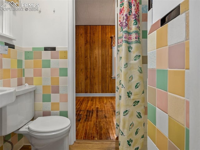 bathroom with wood walls, tile walls, wood-type flooring, and toilet