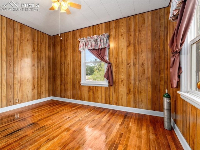 empty room featuring ceiling fan, wood-type flooring, and wooden walls