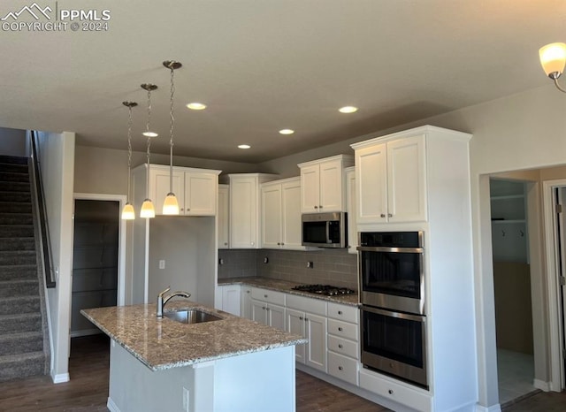 kitchen with appliances with stainless steel finishes, sink, decorative light fixtures, an island with sink, and light stone countertops